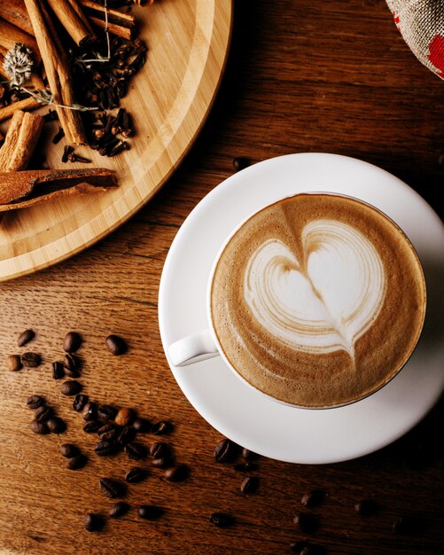 Vista superior de espresso caliente junto con semillas de café y canela en el piso de madera marrón