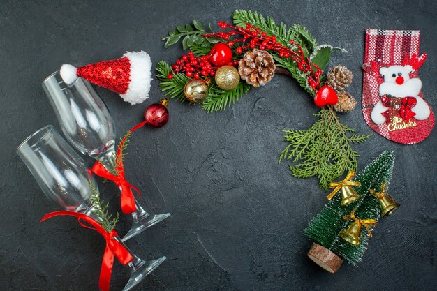 Vista superior del estado de ánimo navideño con copas de cristal caídas ramas de abeto calcetín de árbol de Navidad sombrero de santa claus sobre fondo oscuro