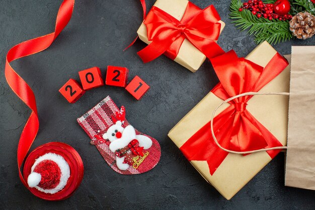 Vista superior del estado de ánimo navideño con hermosos regalos ramas de abeto conífera cono cinta roja y números sombrero de santa claus calcetín de Navidad sobre fondo oscuro