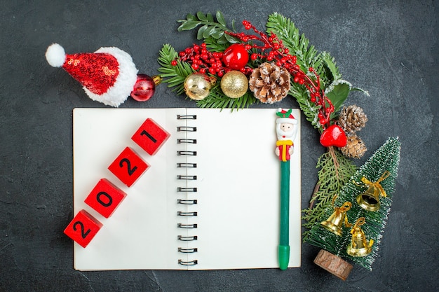 Vista superior del estado de ánimo navideño con ramas de abeto Números de árbol de Navidad de sombrero de santa claus en el cuaderno sobre fondo oscuro