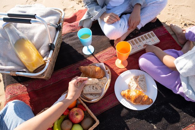 Vista superior de la familia afroamericana en un picnic en la playa. Madre e hijos con ropa informal sentados en una manta, comiendo pan, bebiendo jugo. Familia, relajación, concepto de naturaleza.