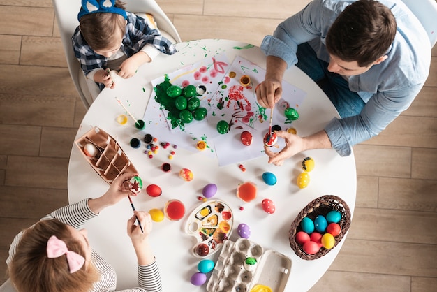 Vista superior familia pintando huevos de pascua juntos