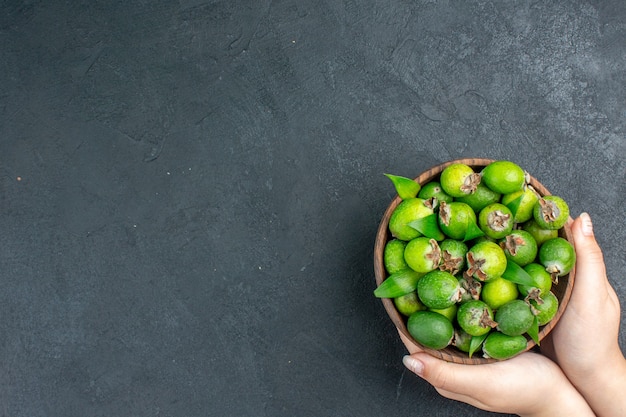 Vista superior de feijoas frescas en balde en mano femenina sobre una superficie oscura con espacio de copia