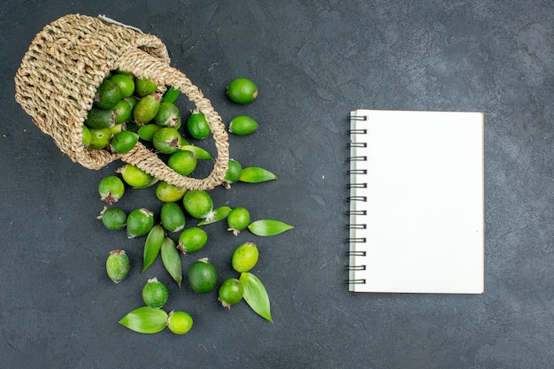 Vista superior de feijoas frescas en la canasta un cuaderno sobre una superficie oscura