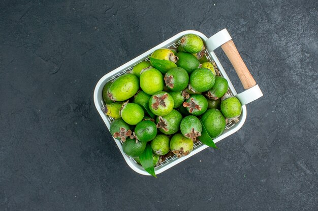 Vista superior de feijoas frescas en canasta de plástico en el espacio libre de superficie oscura