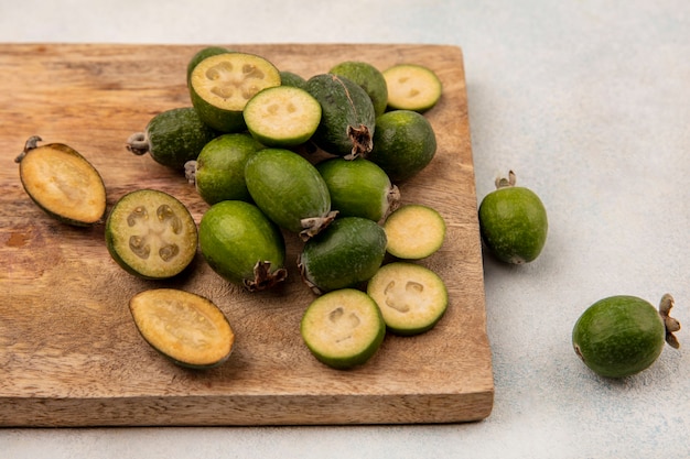 Vista superior de feijoas frescas enteras y cortadas a la mitad aisladas sobre una tabla de cocina de madera sobre un fondo gris