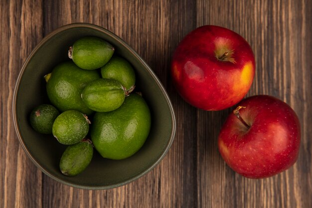 Vista superior de feijoas frescas con limas en un recipiente con manzanas rojas aisladas sobre una superficie de madera