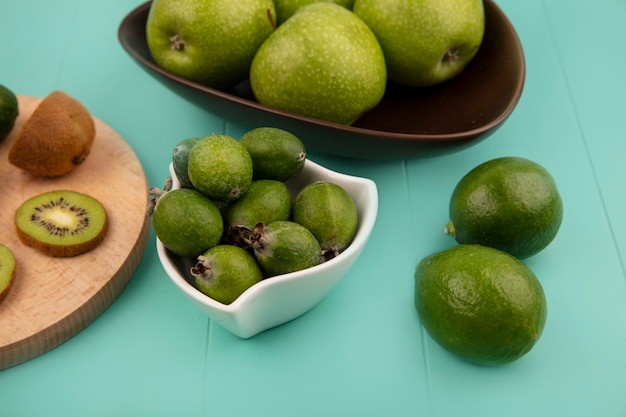 Vista superior de feijoas frescas en un recipiente con manzanas en un recipiente con limas aislado en una pared azul