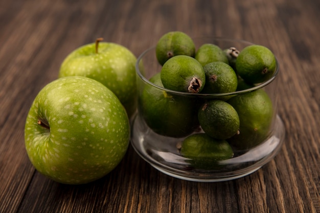 Foto gratuita vista superior de feijoas maduras frescas en un recipiente de vidrio con manzanas verdes aisladas en una pared de madera