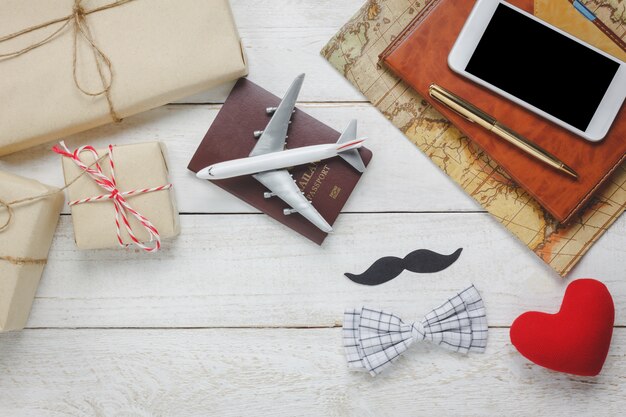 Vista superior Feliz Día del Padre con travel.Airplane y pasaporte en madera rústica background.accessories con, mapa, bigote, corbata de la vendimia, pluma, presente, corazón rojo, teléfono móvil blanco y portátil.