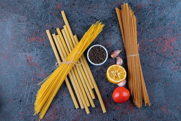 Vista superior de fideos crudos con tomates rojos frescos y ajo sobre una superficie oscura.