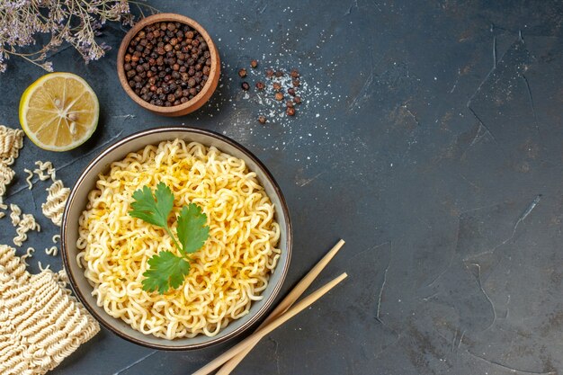 Vista superior de fideos ramen asiáticos en un tazón de pimienta negra en un tazón pequeño, corte los palillos de limón en la mesa oscura