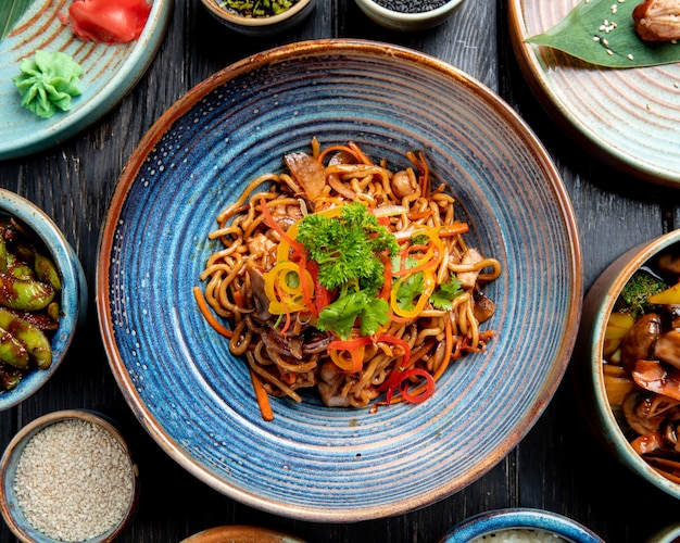 Vista superior de fideos salteados con verduras y camarones en un plato sobre la mesa de madera