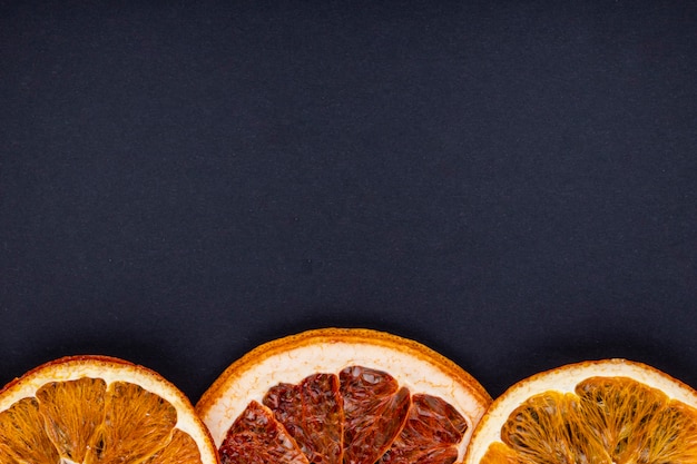 Foto gratuita vista superior de una fila de rodajas secas de naranja y pomelo dispuestas sobre fondo negro