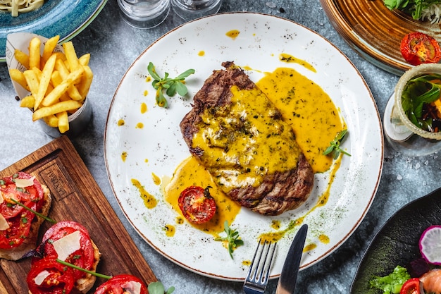 Vista superior filete a la parrilla carne roja con salsa de tomate, menta y papas fritas sobre la mesa