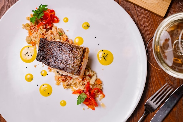 Foto gratuita vista superior del filete de pescado a la parrilla servido encima de la ensalada de cuscús con pimientos