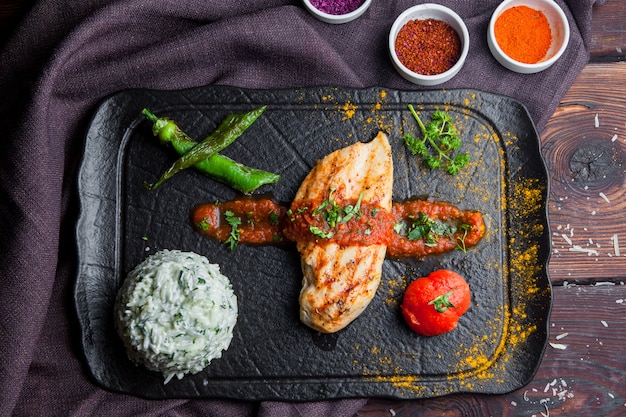 Vista superior filete de pollo a la parrilla con guarnición, tomate, pimiento una mesa de madera oscura