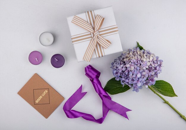 Vista superior de la flor con velas, caja de regalo de cinta y tarjeta de buena suerte sobre fondo blanco.