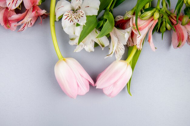 Vista superior de flores de alstroemeria de color blanco y rosa con tulipanes rosados en mesa blanca