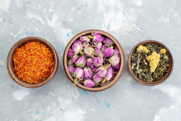 Una vista superior de flores de color púrpura junto con la planta seca de naranja dentro de tazones en la mesa de luz planta de flor seca