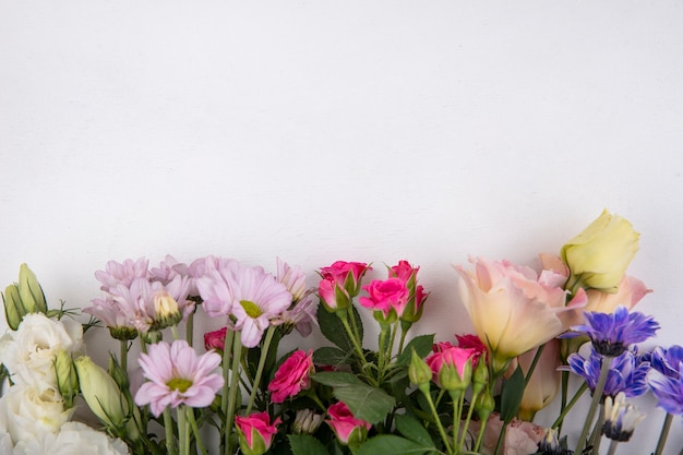 Vista superior de flores coloridas y sorprendentes como rosas y margaritas sobre un fondo blanco con espacio