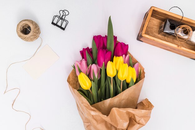 Vista superior de las flores coloridas del tulipán; cuerda; clip de papel; Tarjeta y papel marrón sobre superficie blanca.