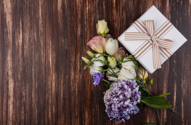 Vista superior de flores frescas como rosas de tulipán gardenzia con caja de regalo aislado sobre un fondo de madera con espacio de copia