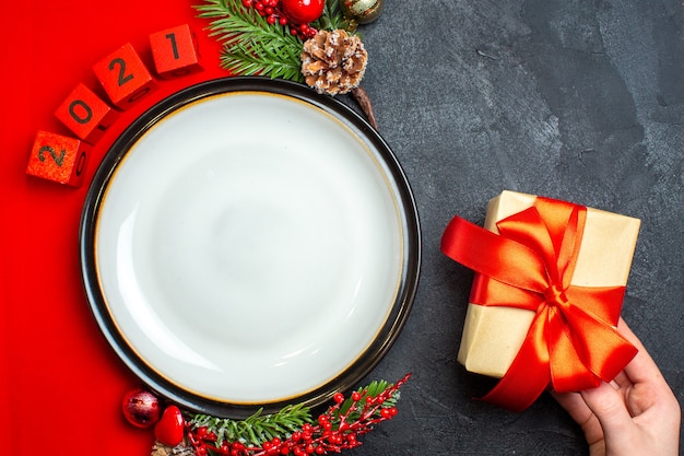 Vista superior del fondo de año nuevo con plato de cena y accesorios de decoración de regalo ramas de abeto y números en una servilleta roja sobre una mesa negra