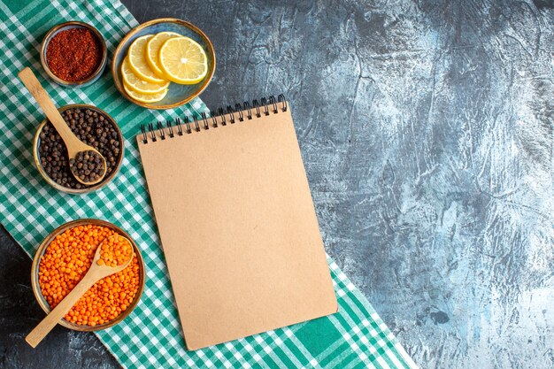 Vista superior del fondo de la cena con diferentes especias, guisante amarillo y cuaderno de espiral en la mesa oscura