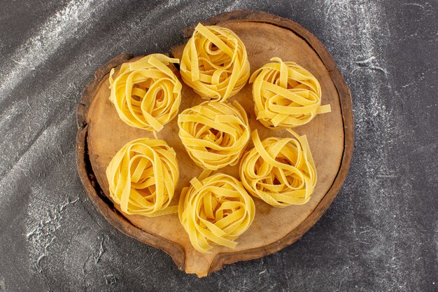 Vista superior en forma de pasta italiana en forma de flor cruda y amarilla en el escritorio de madera marrón espaguetis de comida italiana de color crudo