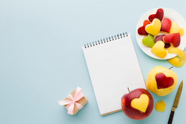 Vista superior de formas de corazón de fruta con cuaderno y presente