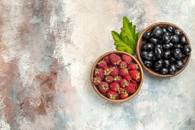 Vista superior de frambuesas y uvas en tazones de hojas sobre una superficie gris aislada con espacio de copia