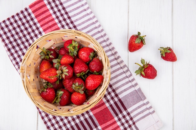 Vista superior de fresas en cesta sobre tela escocesa y superficie de madera