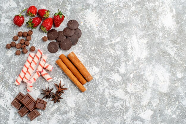 Vista superior fresas chocolates caramelos cereales canela semillas de anís en el lado izquierdo de la mesa gris-blanca con espacio libre