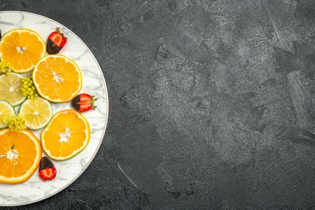 Vista superior de fresas cubiertas de chocolate en rodajas de naranja limón y fresas cubiertas de chocolate en la placa en el lado izquierdo de la mesa oscura