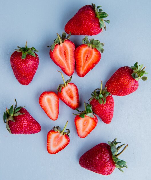 Vista superior de fresas enteras y cortadas en superficie azul