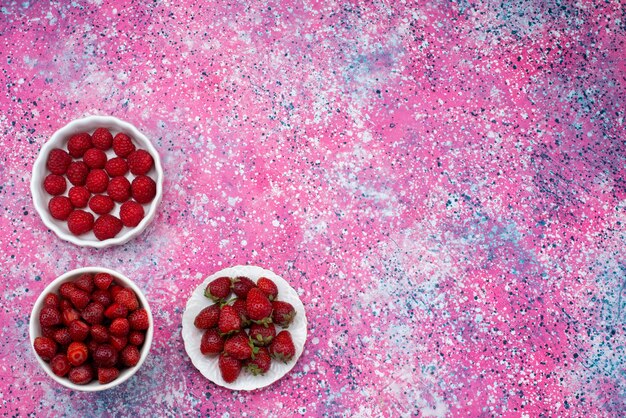 Vista superior de fresas y frambuesas dentro de placas blancas sobre el fondo morado de color baya fresca