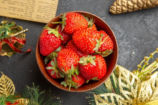 Vista superior de fresas frescas dentro de la placa alrededor de juguetes navideños sobre fondo oscuro