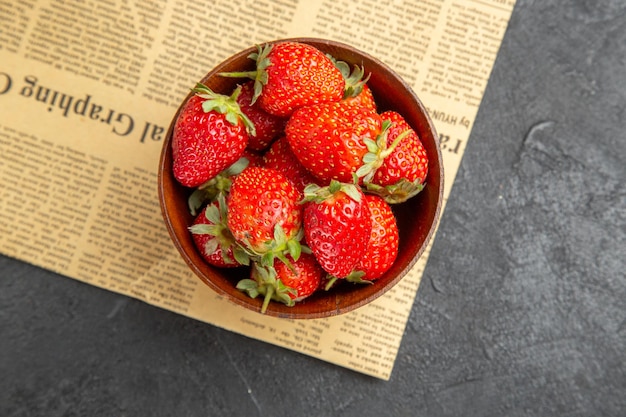 Vista superior de fresas frescas dentro de la placa alrededor de juguetes navideños sobre fondo oscuro