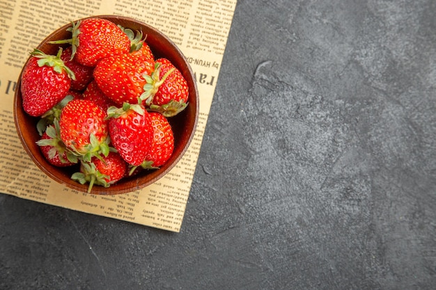 Vista superior de fresas frescas dentro de la placa alrededor de juguetes navideños sobre fondo oscuro