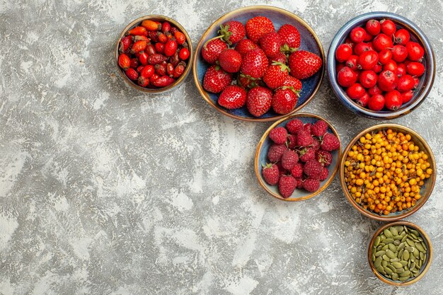 Vista superior de fresas frescas con frutos rojos sobre fondo blanco.