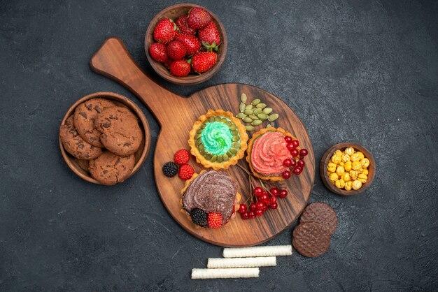 Vista superior de fresas frescas con galletas y pasteles en el pastel de galletas de azúcar de mesa oscura