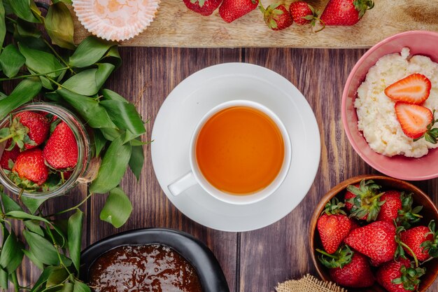 Vista superior de fresas frescas maduras con mermelada de requesón y una taza de té en la mesa de madera rústica