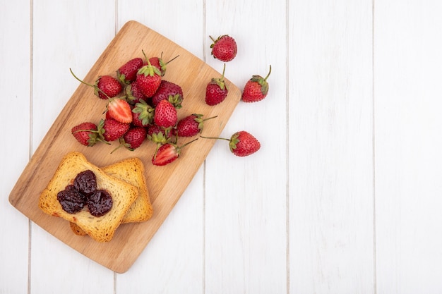 Vista superior de fresas frescas en una tabla de cocina de madera con pan tostado sobre un fondo de madera blanca con espacio de copia