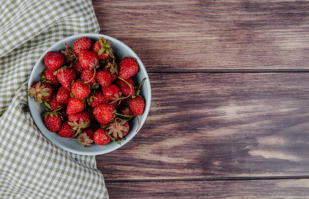 Vista superior de fresas maduras frescas en un recipiente en madera rústica con espacio de copia