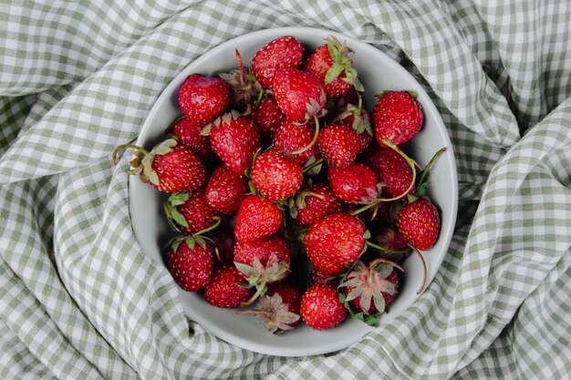 Vista superior de fresas maduras frescas en un recipiente sobre tela escocesa