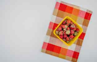 Foto gratuita vista superior de fresas maduras frescas en un tazón amarillo en servilleta a cuadros en blanco con espacio de copia