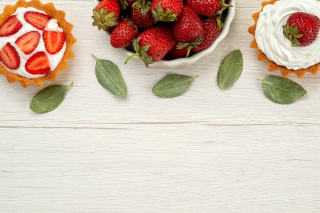 Vista superior de fresas rojas frescas bayas suaves y deliciosas dentro de la placa con tortas en luz, fruta roja baya