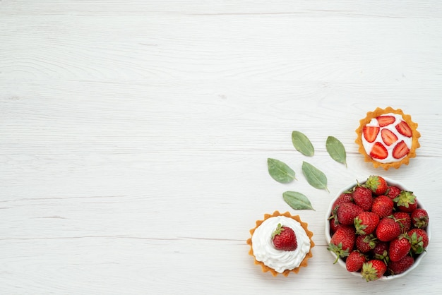 Vista superior de fresas rojas frescas bayas suaves y deliciosas dentro de la placa con tortas en el piso de luz fruta roja fresca