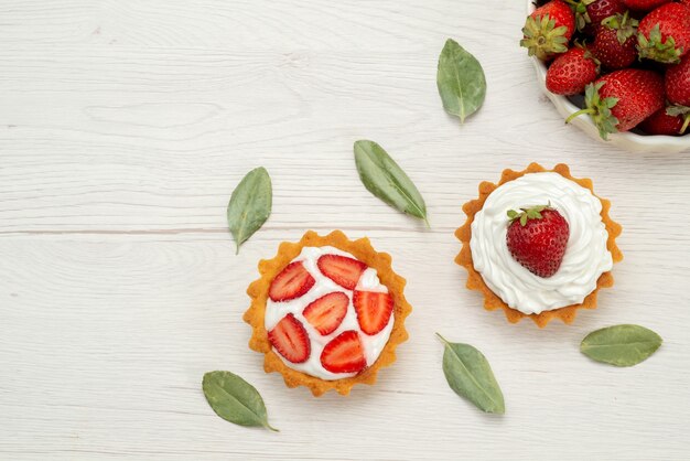 Vista superior de fresas rojas frescas bayas suaves y deliciosas dentro de un plato blanco con tortas en luz, fruta roja baya